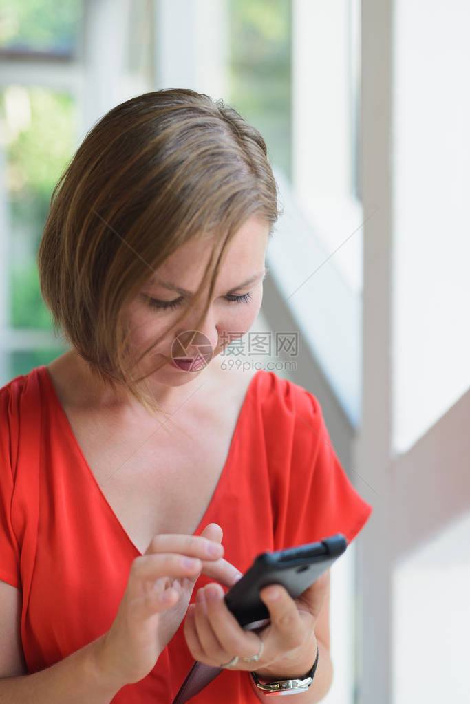身着活珊瑚色洋装的年轻成年女子坐在靠近窗户的咖啡店里图片