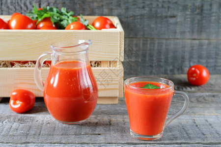 玻璃器皿中的新鲜番茄汁一个玻璃杯的番茄汁和木箱里的新鲜番茄在灰色图片