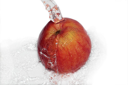 一个成熟的红苹果在干净的水流下清洗飞溅和水滴四处飞舞白色图片
