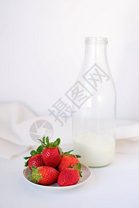在甜点盘上开胃的草莓和一瓶白色背景的新鲜牛奶图片