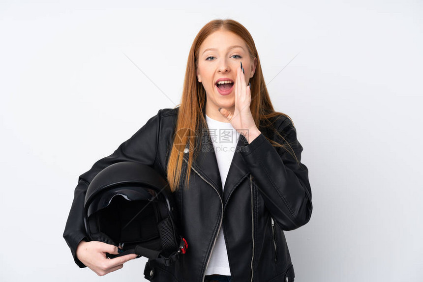 带着摩托车头盔的年轻红发女青年在孤立的白人背景上大喊图片