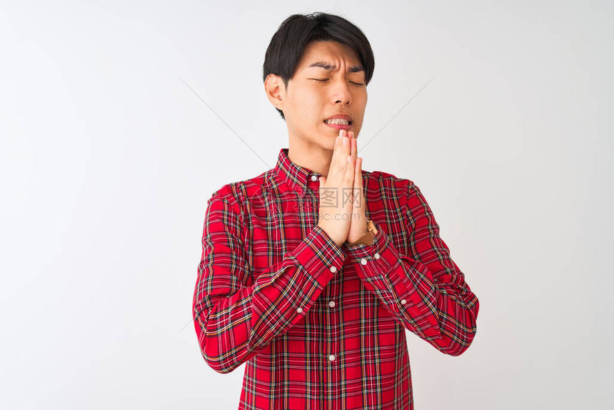 年轻的男子穿着休闲的红衬衫站在孤立的白色背景上乞讨和祈祷图片