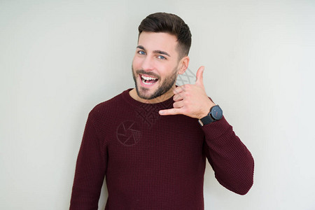 年轻英俊的男人穿着一件毛衣在孤立的背景下微笑着用手和指做电话手势图片