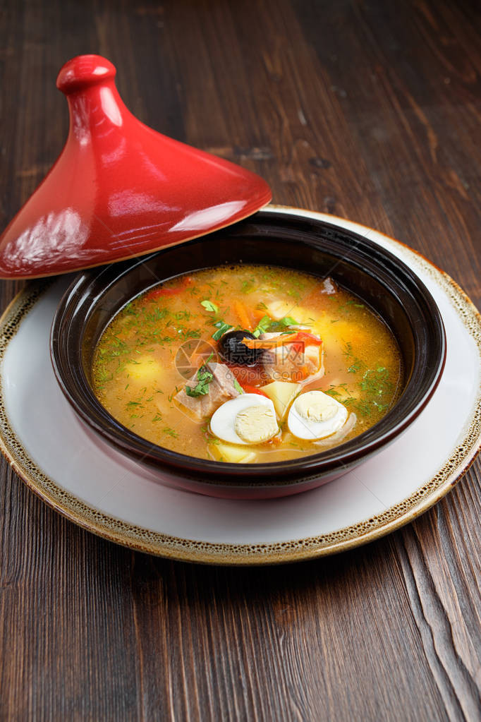 鱼汤在一个锅中一个红盖子在黑木背景图片