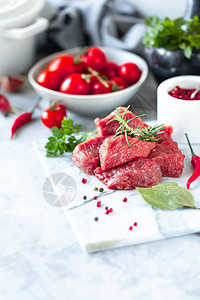 白大理石背景的生鲜肉片西红柿辣椒和烹饪用药图片