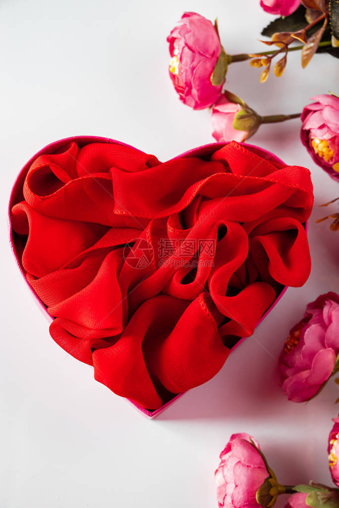 红色心形礼品盒和白色背景上的花朵白色背景上呈心形和粉红色花朵的红色礼图片