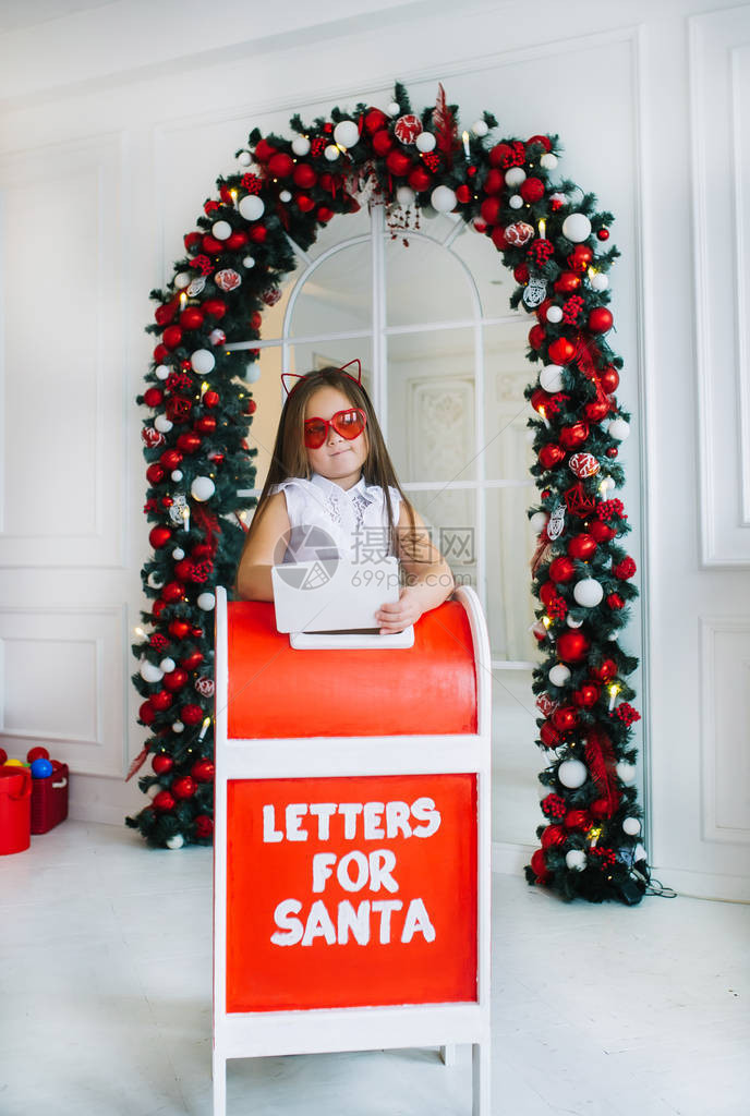 有猫耳朵的风趣小女孩站在室内邮箱附近孩子给圣诞老人写了一封图片