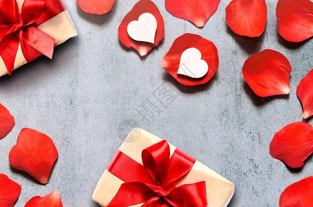 在牛皮纸上的礼物与灰色桌子上的红玫瑰花瓣背景上的心形装饰背景图片