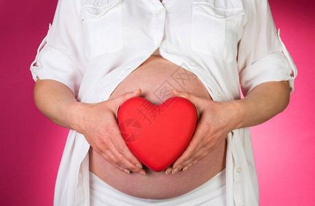 孕妇拿着粉红色背景上的心图片