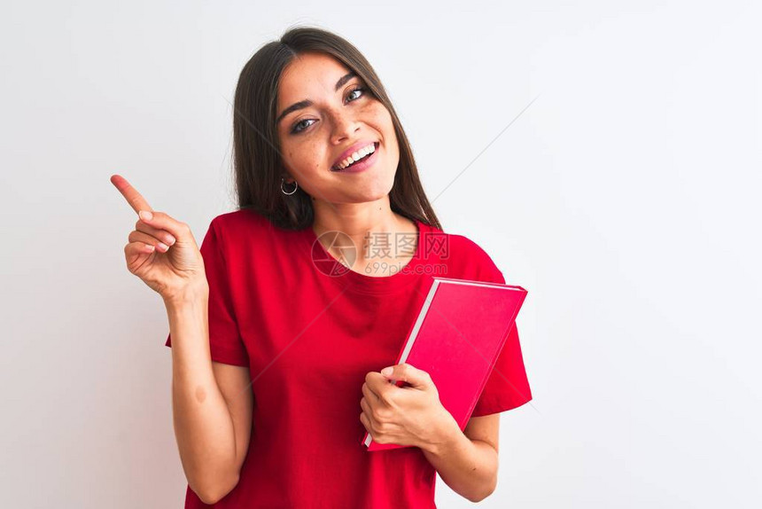 年轻美丽的女学生拿着红书站在孤立的白色背景上快乐地用手和指对着图片