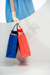 在白色背景圆洞附近持有红色和蓝色购物袋的手套上的时装妇女被切图片