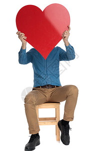 穿着蓝衬衫的年轻男子躲在红色大心脏后面背景图片
