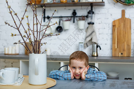 一个忧郁的金发小男孩坐在厨房的桌子旁图片