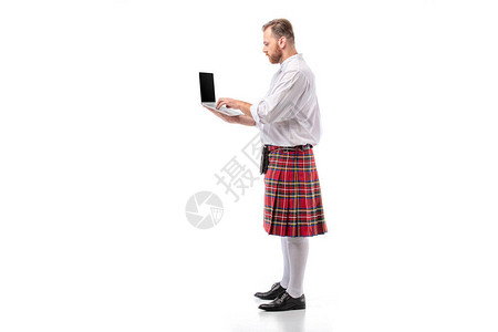 使用白色背景笔记本电脑的红色苏格兰红头男子在红色脚板图片