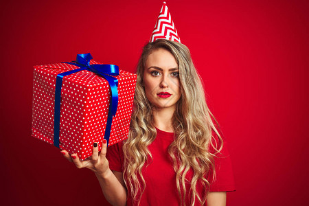 年轻漂亮的女人在红色孤立的背景下拿着生日礼物图片