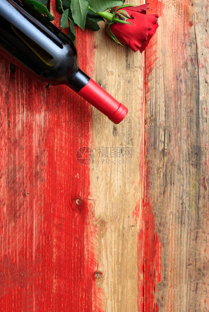 红酒瓶和火情红色玫瑰花在木材图片