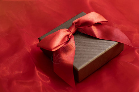 在通风的红色背景上带有缎面蝴蝶结的圣诞礼盒图片