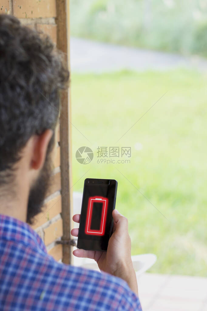 年轻人在屏幕上拿着低电池概念的智能手机的背影所有的图图片