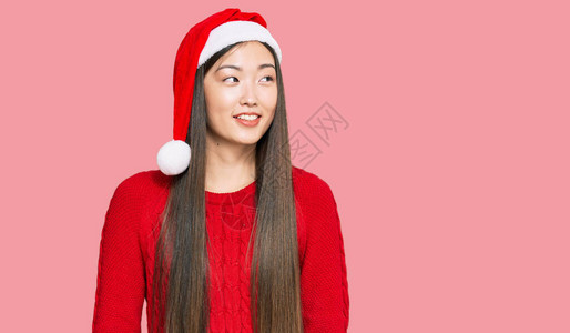 穿着圣诞帽的年轻女人带着笑容自然的表情和自信地微笑而一边看图片