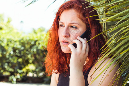 站在户外站着的红头发女孩在手机上聊天时近距离图片