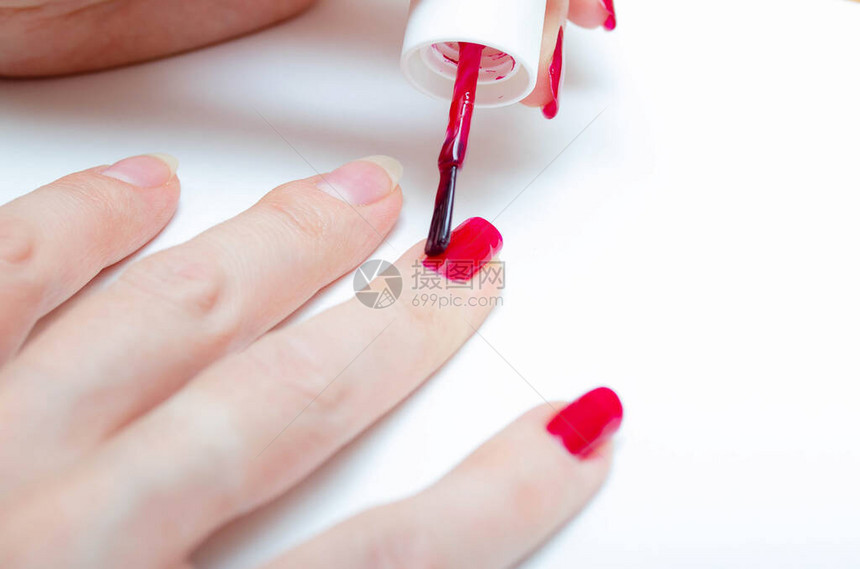 在家修指甲DIY美甲这个女孩把自己的指甲涂成酒红色有光泽的指甲油宏中的宏刷子在白色背景上以强烈的大变焦在指图片