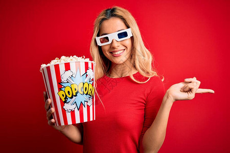 看电影的年轻金发美女以3D杯眼镜吃爆米花作为零食用手和指对图片