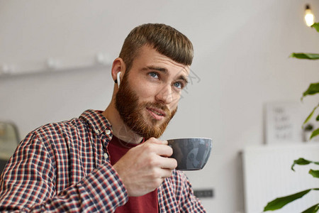 快乐的年轻迷人的姜黄色胡须男子手持灰色咖啡杯的肖像图片