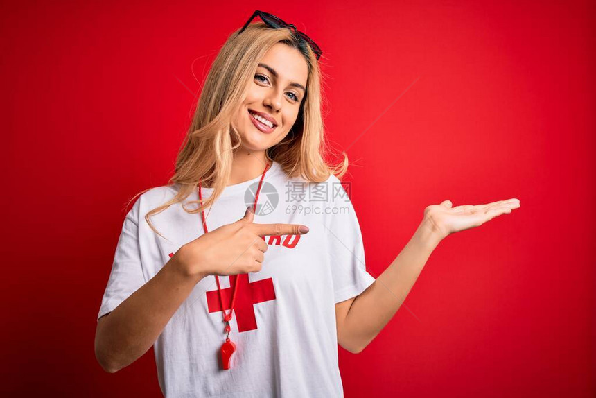 年轻美丽的金发救生员女人穿着t恤与红十字使用口哨惊讶并微笑着对镜头图片