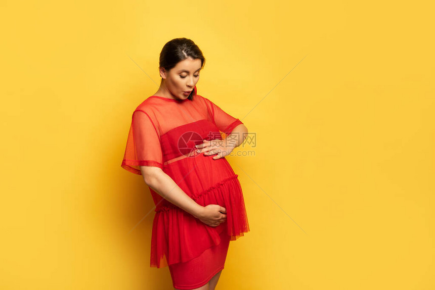 穿着红色束腰外衣的怀孕年轻女子在黄色上摸着肚子图片
