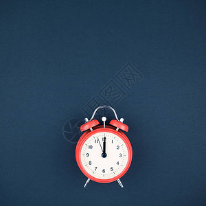 深蓝色纸背景上12点钟的红色复古闹钟的概念图像图片