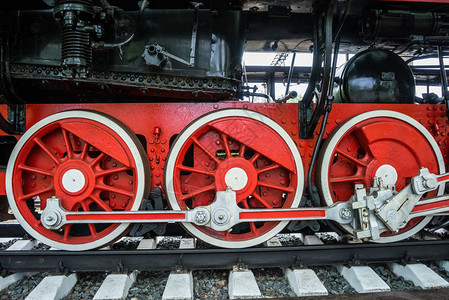 黑色火车背景上有白色轮辋的红色轮子停在博物馆里的旧蒸汽机图片