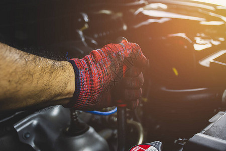 戴红手套的机械手在汽车维修车库使用套筒扳手维修汽车发动机图片