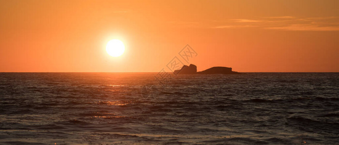 太阳在日落时反射在海洋上地平线上有岩图片