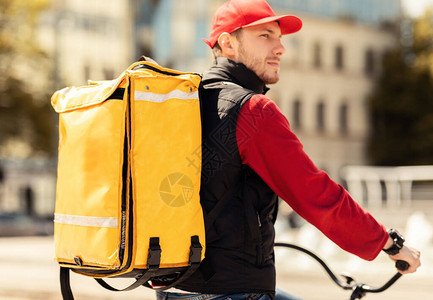 在城市地区骑着自行车外门的盖伊乘车在城市中的黄背包中运送食物空图片