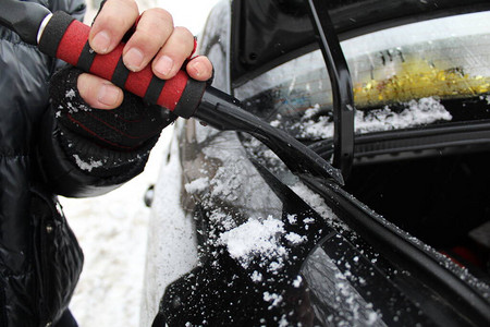 用于在冬天从汽车上清除冰雪的刮板照片一个男人用刮板从雪中清除汽车后备箱打开这辆车是黑色的一个戴着手套的男人的手刷红色和黑图片