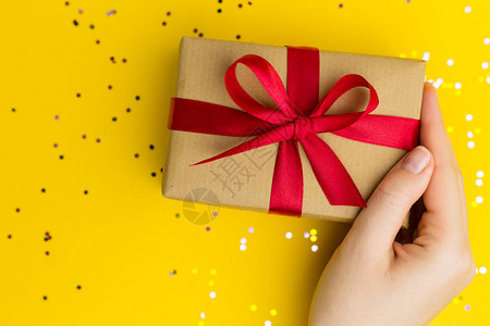 带有红丝带的棕色礼品盒黄色背景圣诞节或生日礼物拿着礼图片