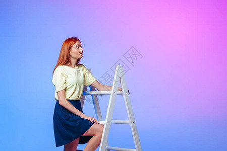 红发女孩在蓝粉色背景下爬楼梯图片