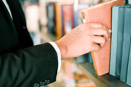 商人或学生手头拿着一本书或在图书馆架背景的书架上挑选一本书商业图片