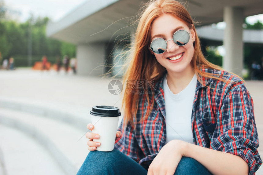穿着圆太阳镜的红发美女笑脸女孩带着一杯咖啡图片