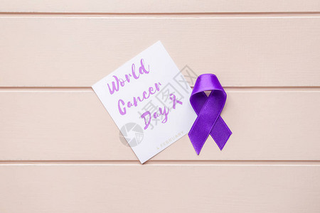 在木质背景上带有文字世界癌症日和紫色丝带的纸图片