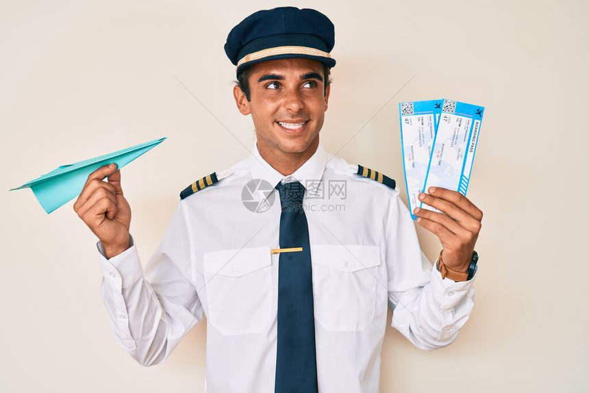 身穿飞机驾驶制服的西班牙年轻人持有纸机和登机牌图片