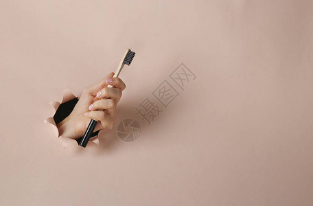 女手中的木牙刷穿过粉红色纸圆洞零废物概念图片