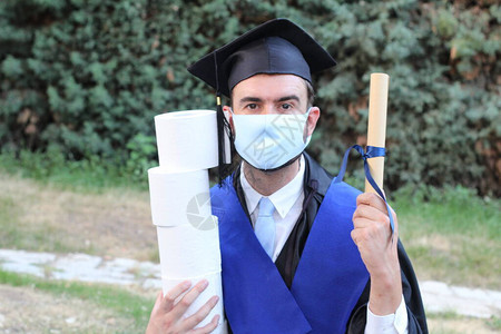 穿着毕业服装的英俊青年学生在公园持有滚版文凭和卫生纸卷的背景图片