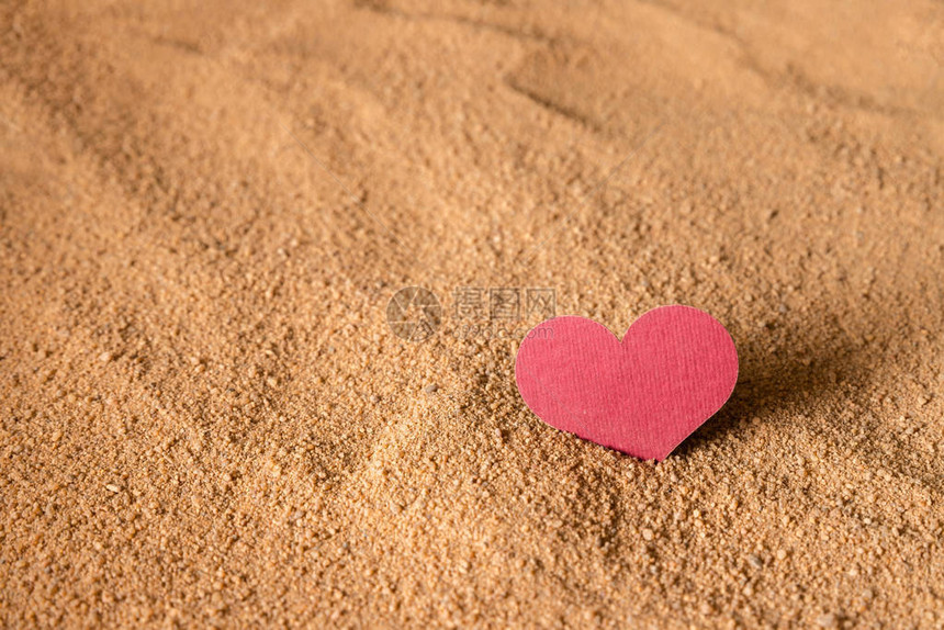 酒红色的心卡在沙质表面图片