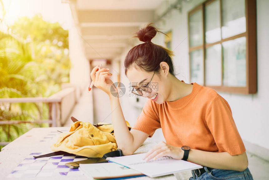 年轻女或亚洲大学生女孩在笔记本上作笔记时微笑地坐着图片