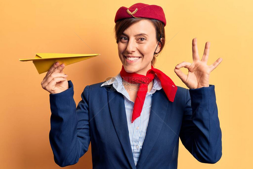 身穿空姐制服的年轻美女拿着纸飞机用手指做好手势图片