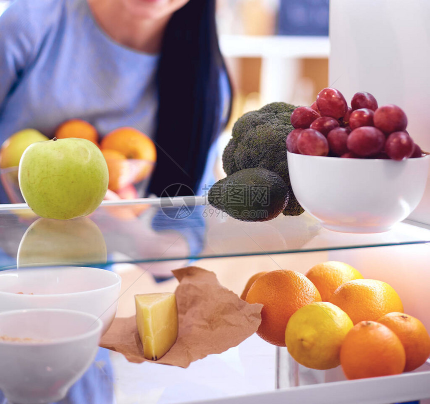 微笑的女人从冰箱里取出新鲜水果健康的食物概念图片