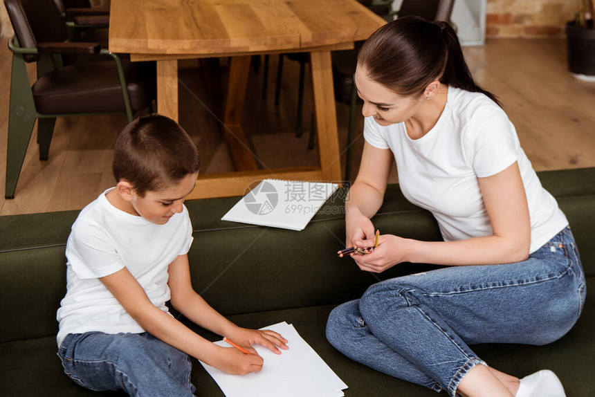 可爱的孩子画在靠近母亲的纸上在沙发上图片