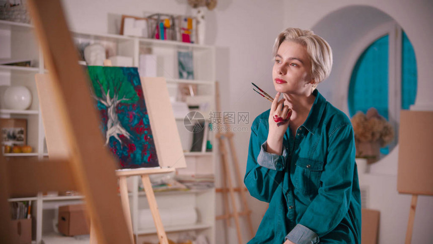 一名年轻的女艺术家在画完之后坐在艺术工作室里图片