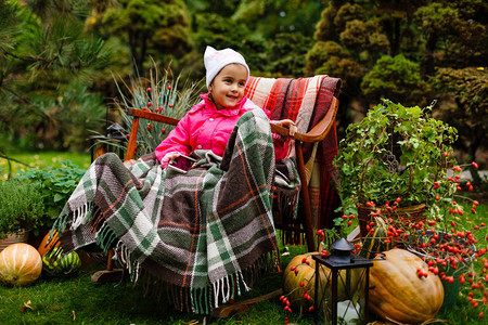 穿着粉红大衣的快乐女孩裹着毛毯坐在秋图片